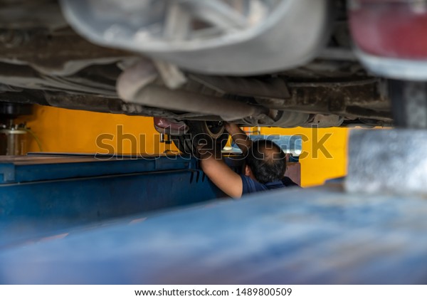 Asian\
Mechanic repairing a lifted car. Fixing car. Balancing the tire of\
the car. A car is lifting to let the Asian mechanic diagnostics the\
suspension of the vehicle to fix or repair\
it.