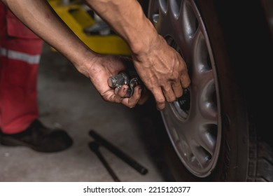 An Asian Mechanic Screws On Lug Nuts Onto The Tire Of A Serviced Car With His Bare Hands. Attaching A Wheel At An Auto Repair Shop.