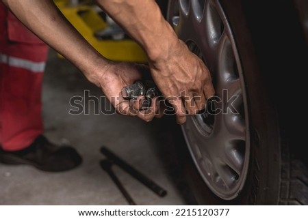 An asian mechanic screws on lug nuts onto the tire of a serviced car with his bare hands. Attaching a wheel at an auto repair shop.