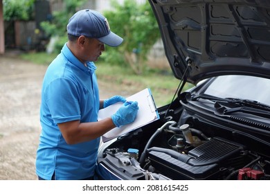 Asian Mechanic Is Writing Something On Paper Clipboard During Checking Car Engine. Concept : Car Maintenance Service At Home.