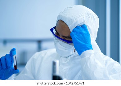 Asian Medical Scientist Wearing Protective White Jumpsuit And Face Mask With Glasses Testing Sample With Microscope In Clinical Laboratory