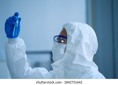 Asian Medical Scientist Wearing Protective White Jumpsuit And Face Mask With Glasses Testing Sample With Microscope In Clinical Laboratory