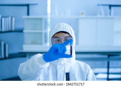 Asian Medical Scientist Wearing Protective White Jumpsuit And Face Mask With Glasses Testing Sample With Microscope In Clinical Laboratory