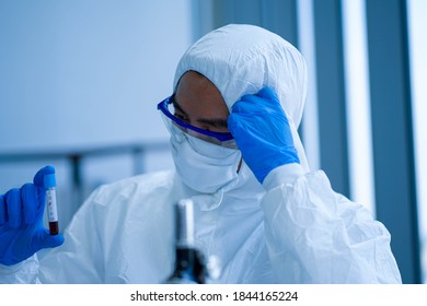 Asian Medical Scientist Wearing Protective White Jumpsuit And Face Mask With Glasses Testing Sample With Microscope In Clinical Laboratory