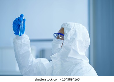 Asian Medical Scientist Wearing Protective White Jumpsuit And Face Mask With Glasses Testing Sample With Microscope In Clinical Laboratory