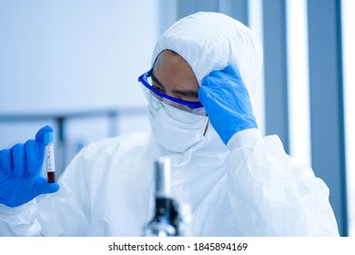 Asian Medical Scientist Wearing Protective White Jumpsuit And Face Mask With Glasses Testing Sample With Microscope In Clinical Laboratory