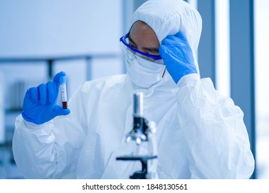 Asian Medical Scientist Wearing Protective White Jumpsuit And Face Mask With Glasses Testing Sample With Microscope In Clinical Laboratory