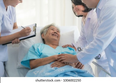 Asian Medical Team Of Doctors Examining And Talking To Asian Elderly Woman Patient, Health Care People Take Note On Clipboard In Hospital. Elderly Patient Care And Health Lifestyle, Medical Concept.