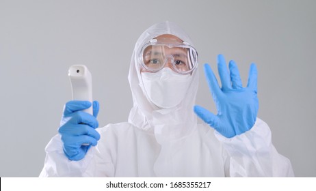 Asian Medical Worker Scanning With Infrared Thermometer, IR Thermo Scan, Confident Asian Doctor In Protective PPE Suit Wearing Face Mask And Eyeglasses