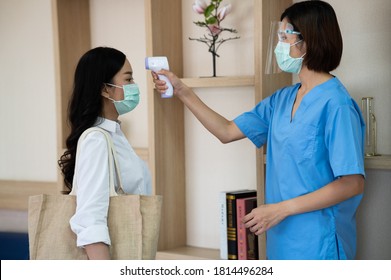 Asian Medical Worker Wear Surgical Face Mask And Face Shield Using Thermometer To Check  Temperature At Patient Who Visit Doctor At Hospital For Against The Spread Of COVID-19