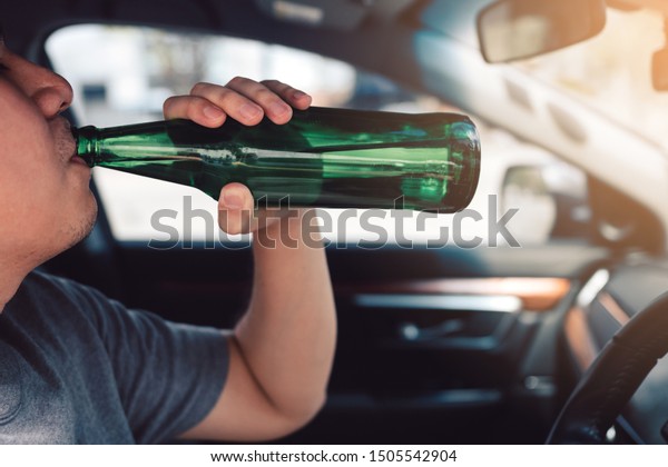 Asian men are breaking the\
traffic rules by holding a bottle of beer and drinking while\
driving.