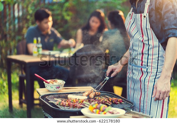 アジアの男性が バーベキューを食べるために友達のグループのために料理を作っている の写真素材 今すぐ編集