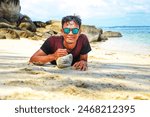 Asian men enjoying the beautiful white sand beach. clean water. fresh air. with a view of the big rocks. wide sea water. blue sky. and the greenery of the trees