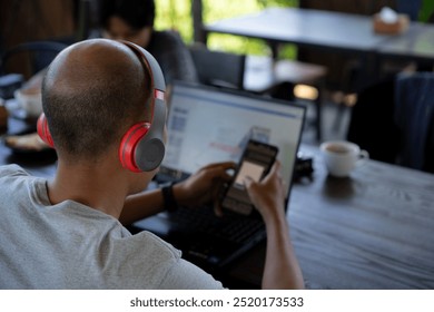 Asian men listen to music using a handset while conducting mobile banking transactions using a cell phone while working remotely at a cafe, concept of remote working, working flexibly from anywhere - Powered by Shutterstock