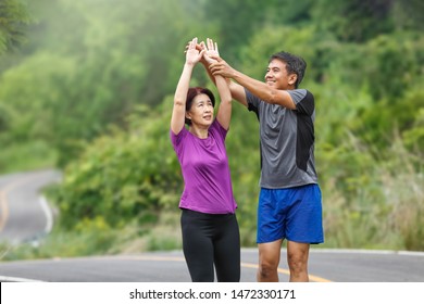 Asian Middle Aged Couple Stretching Muscles Before Jogging In Park