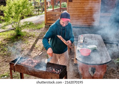 Asian Middle Aged Man Cooking Chicken Meat On Barbecue Grill In Backyard.