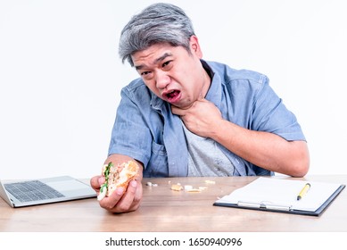Asian middle aged man having symptoms of food stuck in his throat Since he eats hamburgers in a hurry While working on a wooden table, On white background, to health care and food concept.