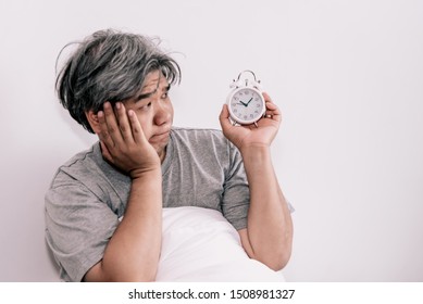 Asian middle aged man just waking up looking at the alarm clock Held in the hand, with white backgroun, concept to was not enough rest time. - Shutterstock ID 1508981327