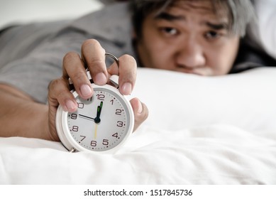 Asian middle aged man just waking up looking at the alarm clock Held in the hand, on white bed in the bedroom, concept to was not enough rest time and This picture focuses on alarm clock - Shutterstock ID 1517845736