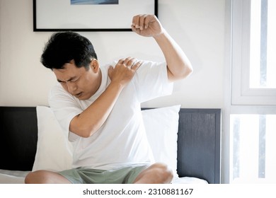 Asian middle aged man suffering from frozen shoulder,pain and stiffness,unable to move,difficulty lifting his arm,male people with calcific tendonitis or shoulder injuries,health care,medical concept - Shutterstock ID 2310881167