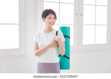 Asian middle aged sportswoman with the yoga mat smiling indoor - Powered by Shutterstock