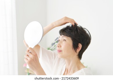 Asian Middle Aged Woman Checking Her Hair Withe Mirror At Home