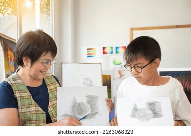 Asian middle-aged female art teacher is explaining the process of pencil drawing, sketching and shading to her male student in her art classroom, raising teens and adult helps kid works concept. - Powered by Shutterstock