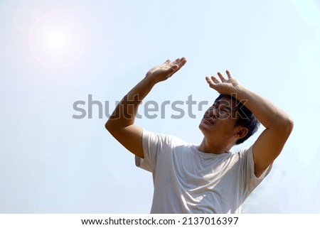Asian middle-aged man feels hot, stands outdoor in sunny day. Concept : hot weather in summer, high temperature. Global warming. Heat wave. Uncomfortable feeling.      