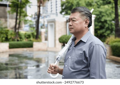 Asian middle-aged man holding umbrella, after raining, rainfall in rainy monsoon season, concept image for weather forecast, Meteorological phenomenon,  precipitation, El Nino - Powered by Shutterstock