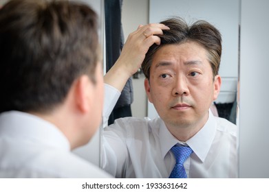 Asian Middle-aged Man Looking In The Mirror And Touching His Hair