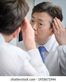 Asian middle-aged man looking in the mirror and touching his hair