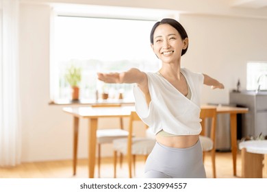 An Asian middle-aged woman is doing yoga in her living room at home. - Powered by Shutterstock