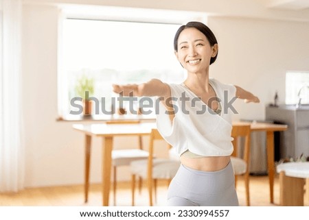 An Asian middle-aged woman is doing yoga in her living room at home.