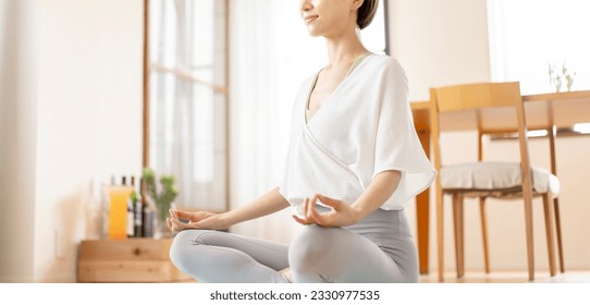 Asian middle-aged woman meditating in her living room. - Shutterstock ID 2330977535