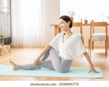 An Asian middle-aged woman is stretching  in the living room at home. - Powered by Shutterstock