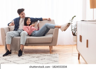 Asian Millennial Couple Using Smartphones Relaxing Sitting On Couch At Home On Weekend. Gadget Lifestyle, Mobile Application, Phone Users Browsing Internet Concept. Empty Space