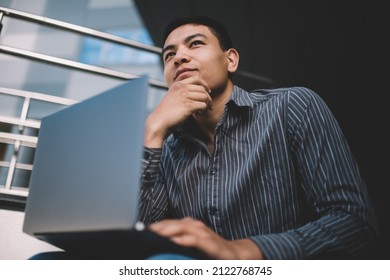 Asian millennial guy thinking about something while working on laptop outdoor. Concept of freelance and remote work. Idea of modern successful man. Young male person near office building. Sunny day - Shutterstock ID 2122768745