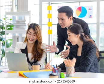 Asian Millennial Professional Successful Male Businessman Mentor In Black Formal Suit Standing Helping Two Female Employee Sitting Working With Laptop Computer At Workstation In Company Meeting Room.