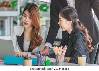 Asian Millennial Professional Successful Male Businessman Mentor In Black Formal Suit Standing Helping Two Female Employee Sitting Working With Laptop Computer At Workstation In Company Meeting Room.