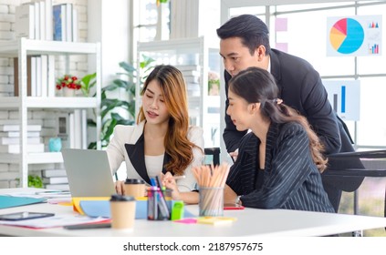 Asian Millennial Professional Successful Male Businessman Mentor In Black Formal Suit Standing Helping Two Female Employee Sitting Working With Laptop Computer At Workstation In Company Meeting Room.