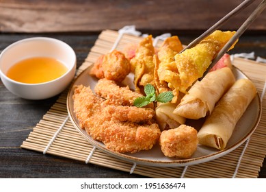 Asian Mixed Deep Fried Food (chicken, Spring Roll, Wonton And Crab Stick) Eating With Chili Sauce By Chopsticks On Wooden Table