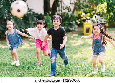 Asian and mixed race happy young kids running playing football together in garden. Multi-ethnic children group, outdoor sport exercising, leisure game activity, or childhood fun lifestyle concept