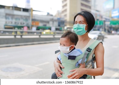 Asian Mom Carrying Her Baby By Hipseat Walking With Wearing A Protection Mask Against Air Pollution In Bangkok City. Thailand.