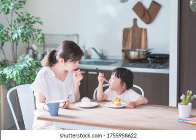 Asian Mom And Daughter Eating Cake At Dining Table At Home