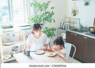 Asian Mom And Daughter Eating Cake At Dining Table At Home