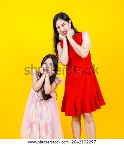 Asian mom and daughter taking portrait photo together on yellow background with funny and lovely.