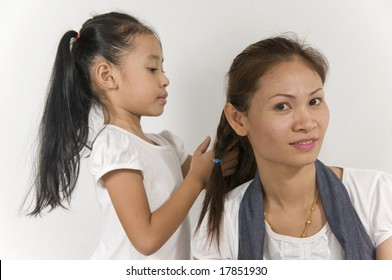 Asian Mom is having her hair braided by her daughter