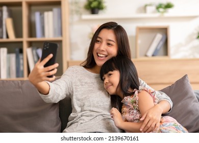 Asian Mom And Her Kid Are Calling On Smartphone. Both Happy Using Cellphone For Video Call Smiling Mom And Girl Having Fun Greetings Online With Making Video Call Communication Through Application.