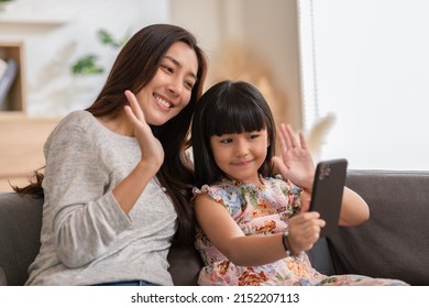 Asian Mom And Her Kid Are Calling On Smartphone. Both Happy Using Cellphone For Video Call Smiling Mom And Girl Having Fun Greetings Online With Making Video Call Communication Through Application.