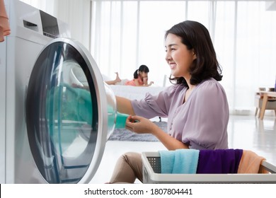 Asian mom loading cloth to washing machine doing laundry at home